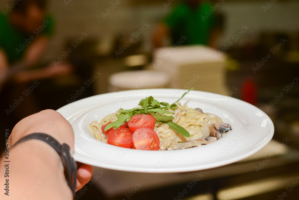 Traditional Italian pasta with tomato sauce and cherry tomatoes served in white plate in a hand of a waiter. Traditional Italian pasta with tomato sauce and cherry tomatoes served in white plate in a hand of a waiter.