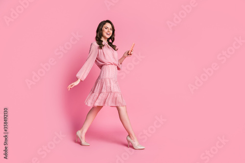 Full length profile side photo of positive cheerful girl lady use smartphone chatting go walk free time wear polka-dot outfit shoes isolated over pastel color background