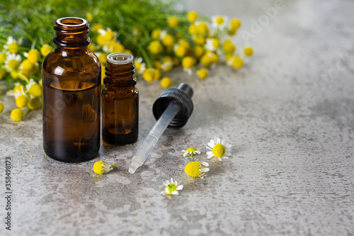 Medical oil bottles and chamomile plant bloom herbs on a stone background photo