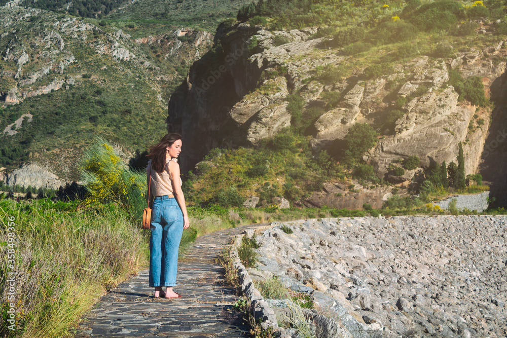 Naklejka premium Beautiful woman on holiday in the mountains in summer walking along a rustic stone path. Selective focus