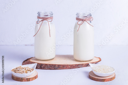 Rice and oat vegan milk in glass bottles on a wooden stand on a white background photo