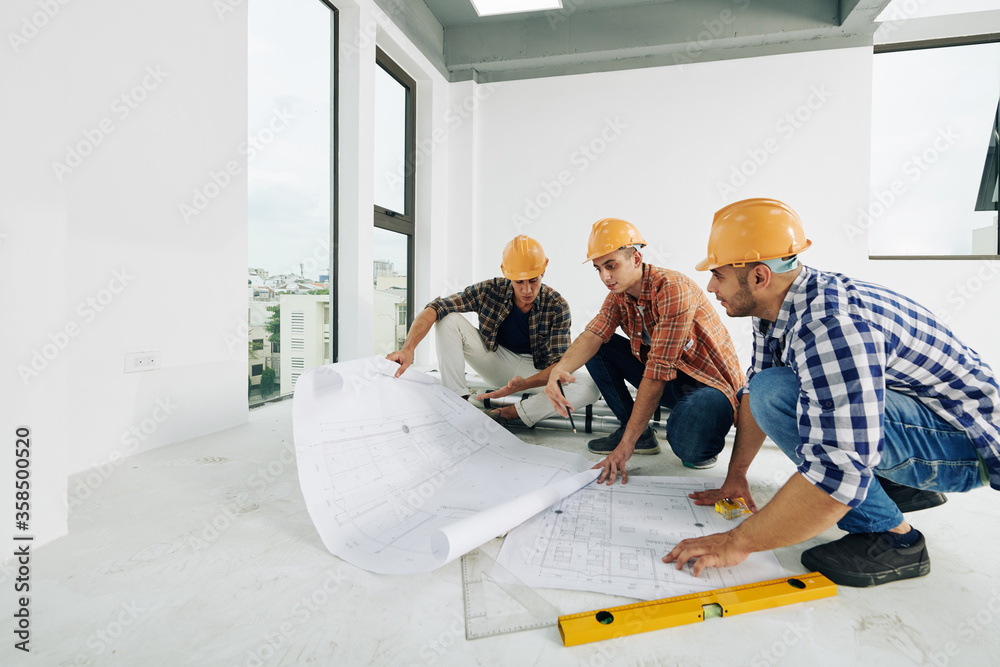 Middle Eastern construction engineers sitting on hunkers in empty room of unfinished building working together on building plan, copy space Middle Eastern construction engineers sitting on hunkers in empty room of unfinished building working together on building plan, copy space