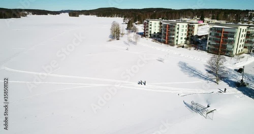 Aerial view around people walking on a trail on snow covered ice, on lake Siilinsalmi, sunny day, in Kallavesi, Kuopio, Finland - pan, drone shot photo