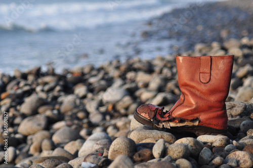 Old single leather boot on the stone beach