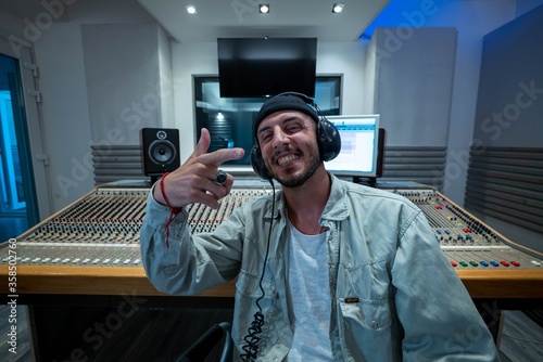 A happy professional male sound producer is smiling satisfied in camera while recording a new song with young singer in a music studio.