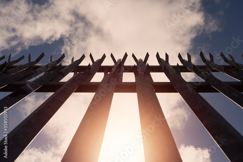 Konstfotografi Metal industrial security fence with spikes on top against blue sky background