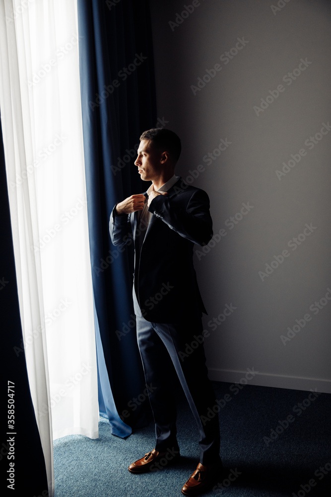 Handsome brutal groom in blue suit near the window Handsome brutal groom in blue suit near the window