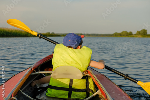 A little boy kayaks on the river in the summer and rowing an oar.