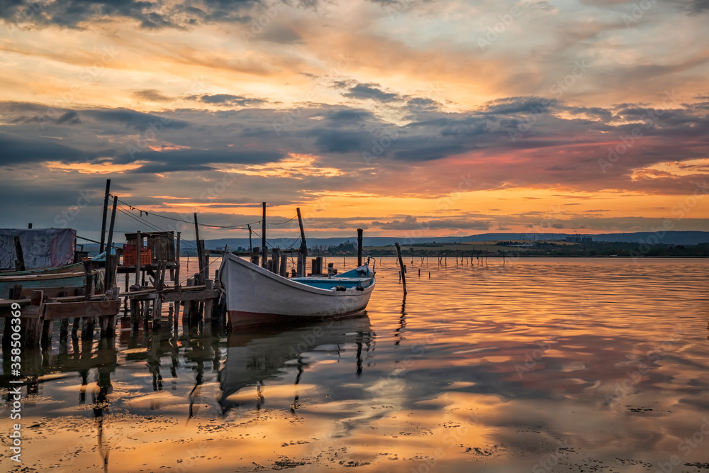 Fototapeta premium amazing colorful sunset at a lake with a boat at a wooden pier. Horizontal view