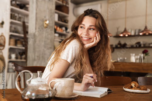 Beautiful young smiling girl sitting at the kitchen table photo