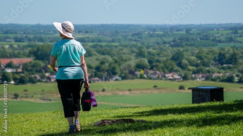 Woman walking towards a large landscape in  Wittenham Clumps, UK with bags in her hand photo