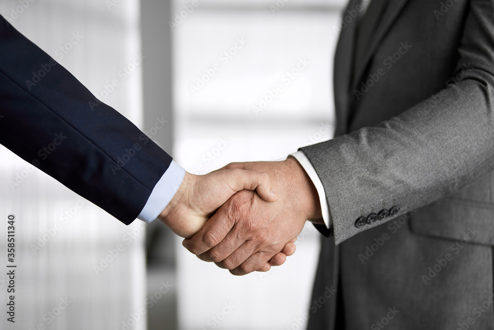 Business people in office suits standing and shaking hands, close-up. Business communication concept. Handshake and marketing