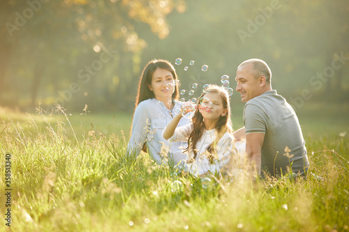 happy family with child girl blow soap bubbles outdoor in sunny summer day