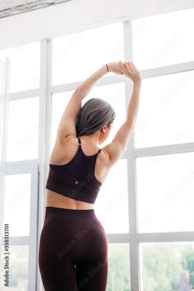 Girl does exercises, stretching, yoga, on a rug near the window, yoga suit, body, slimness and health