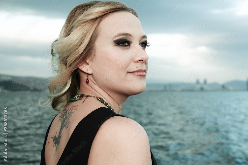 young woman with a tattoo on her back, standing by the sea