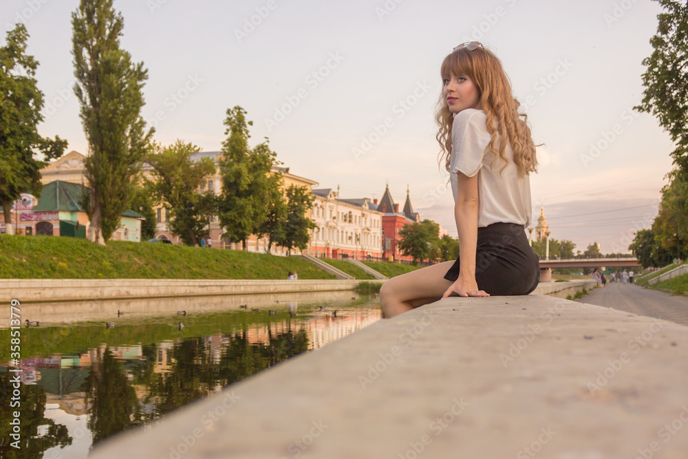 Embankment of the city of Orel. A girl sits on a fence by the river.