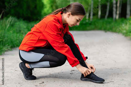 young girl tying shoelaces before running on a summer forest trail