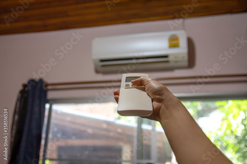 Woman hand holding remote control directed to air conditioner adjust cold temperature, close up.