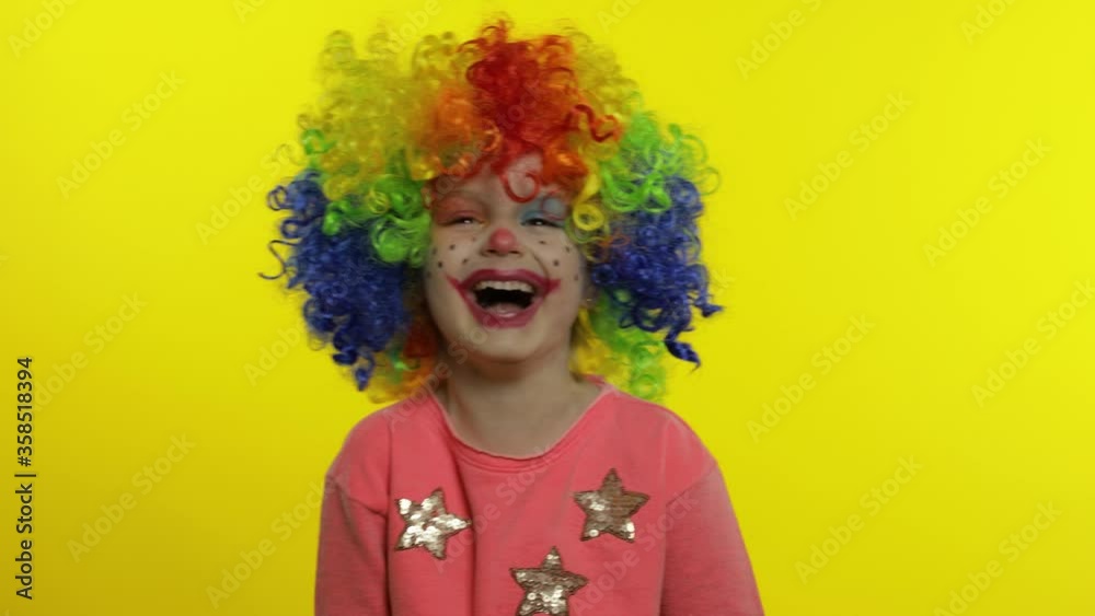 Little child girl clown in rainbow wig making silly faces. Having fun, smiling, laughing. Halloween Little child girl clown in rainbow wig making silly faces. Having fun, smiling, laughing. Halloween