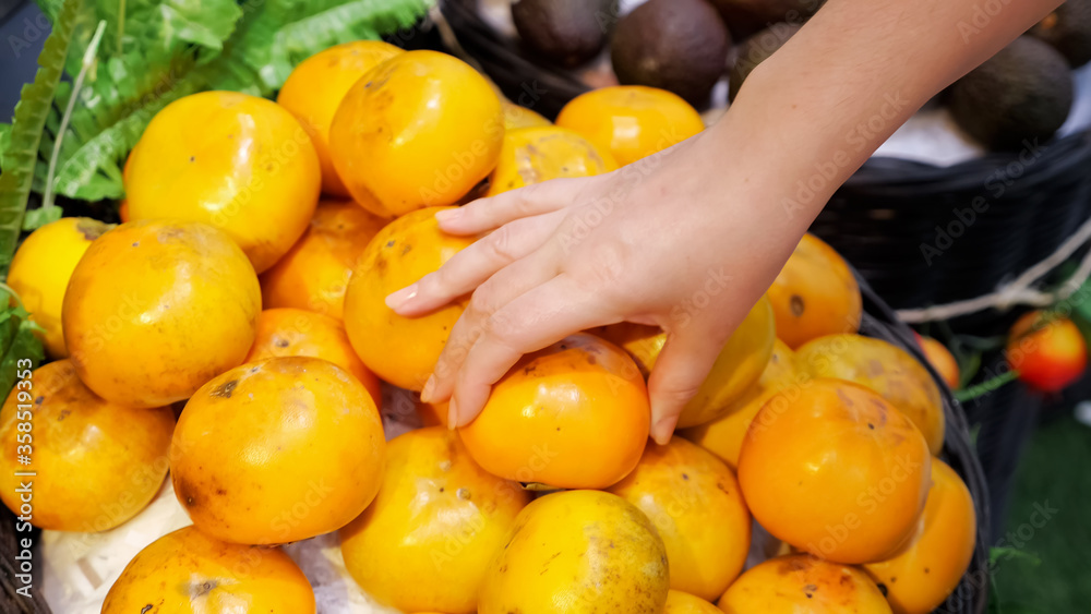Woman's hand picks persimmons in a store.