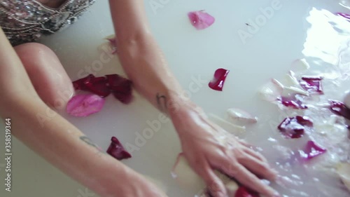 A young naked girl bathes in a bath with milk and pink rose petals. Naked slender wet female legs