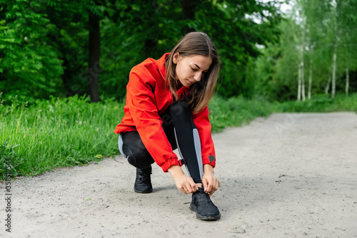 young girl tying shoelaces before running on a summer forest trail © Yevhenii Rukavitsyn