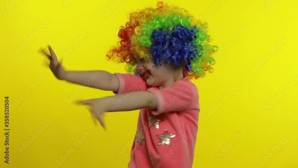 Little child girl clown in colorful wig waving hands, having fun, smiling. Halloween Little child girl clown in colorful wig waving hands, having fun, smiling. Halloween