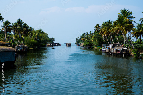 Obraz na płótnie Small houses in a local village located next to Kerala's backwater on a bright sunny day and traditional Houseboat seen sailing through the picturesque backwaters of Allapuzza or Alleppey in Kerala w salonie