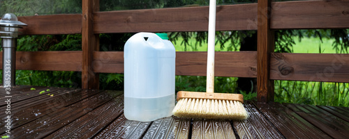 Brush and plastic canister with detergent on a wooden board, wooden terrace. Technologies and tools for cleaning surfaces.