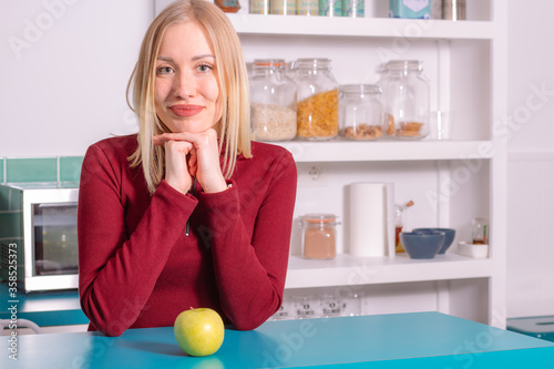 Happy young woman in the kitchen with green apple on the table