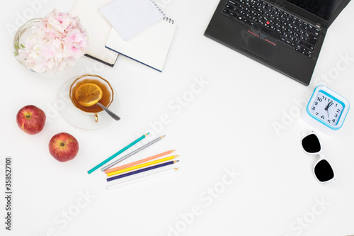 Laptop, notebook, felt-tip pens, watches, sunglasses, a cup of tea with lemon, pencils and a bouquet of hydrangea on the office desk