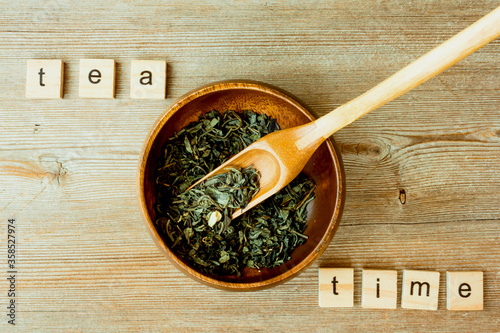 Tea time inscription, Chinese, Japanese green dried tea leaves at bamboo scoop and bowl on table