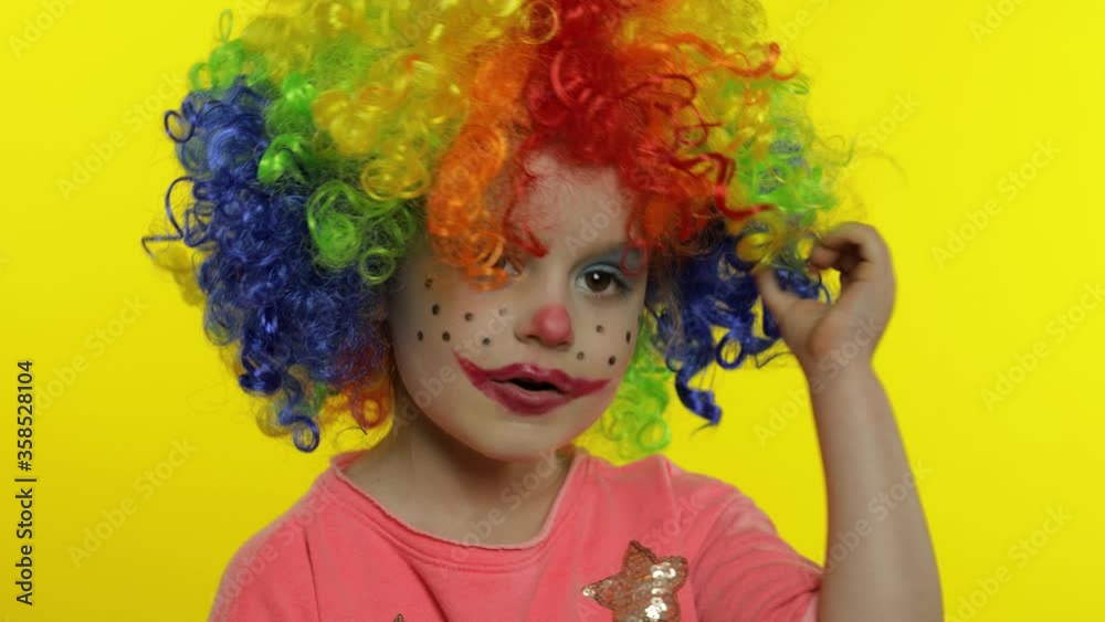 Little child girl clown in colorful wig tells something interesting, having fun, smiling. Halloween Little child girl clown in colorful wig tells something interesting, having fun, smiling. Halloween