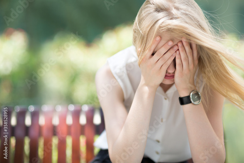 Φωτογραφία Depressed young woman crying alone and covering her face while sitting alone on park bench during sunny summer day