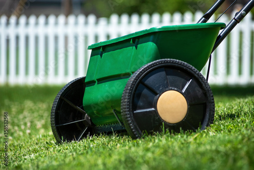 Close-up isolated lawn chemical grass seed and fertilizer spreader in yard with white picket fence in background photo