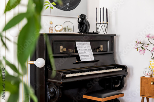 Modern composition of home interior with stylish black piano, design furnitures, plants, decoration, flowers, mock up painitngs and elegant personal accessories in trendy home decor. photo