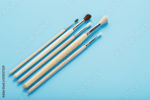 Brushes for drawing with paints made of natural wood and wool on a blue background.