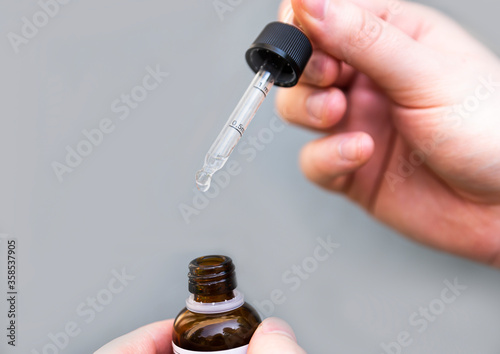 The person holds the bottle in his hand and takes a dose of the medicine with a dropper