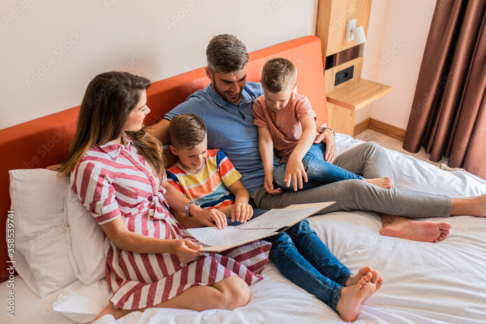 Family of four enjoying together at hotel room, sitting at bed reading hotels offers. Family of four enjoying together at hotel room, sitting at bed reading hotels offers.