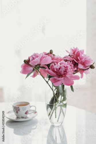 pink peonies on the table with a cup of tea