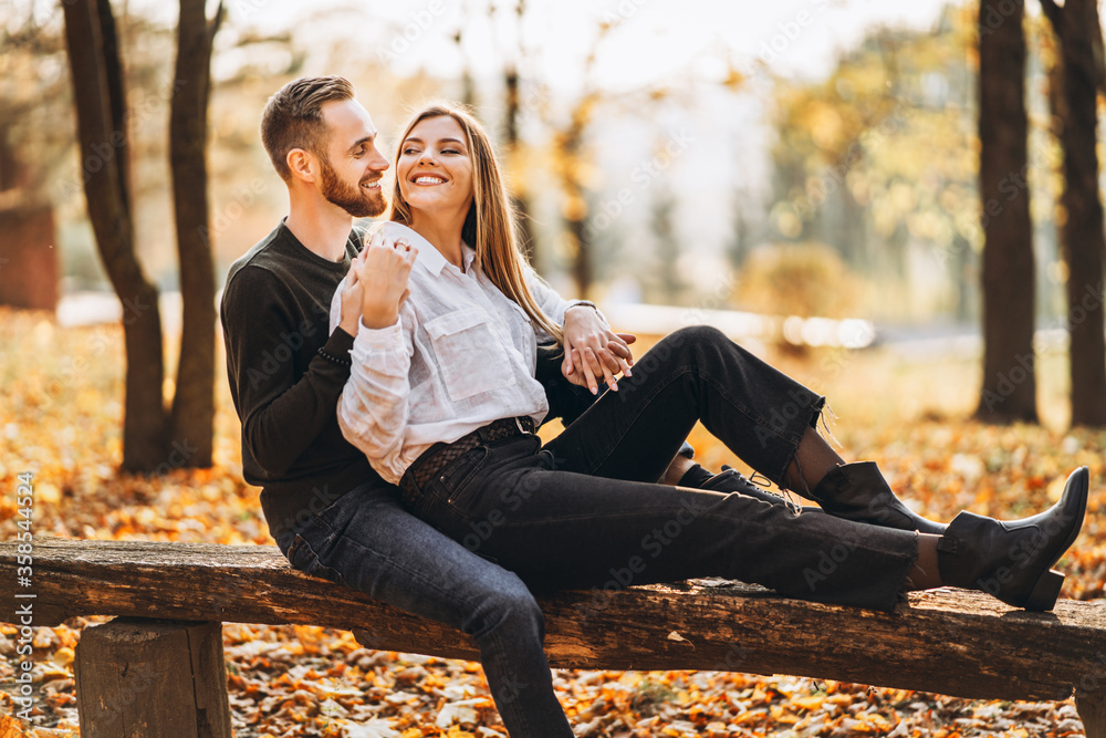A young loving couple sitting on a wooden bench in the forest. Man and woman hugging and smiling on the background of autumn trees A young loving couple sitting on a wooden bench in the forest. Man and woman hugging and smiling on the background of autumn trees