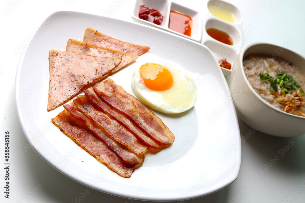 Rice Porridge, ham, bacon, fried egg, served with various sauces Put on the white table Ready to eat Rice Porridge, ham, bacon, fried egg, served with various sauces Put on the white table Ready to eat