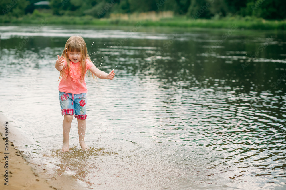 A happy little girl stands barefoot in the water and raises the water with her hands. Copy space A happy little girl stands barefoot in the water and raises the water with her hands. Copy space