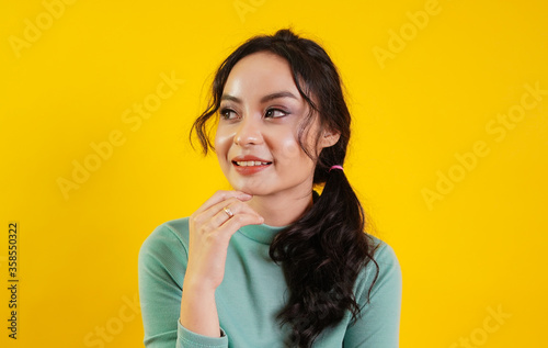 Portrait of Asian teenage beautiful cute cheerful girl smiling looking at camera over yellow background.