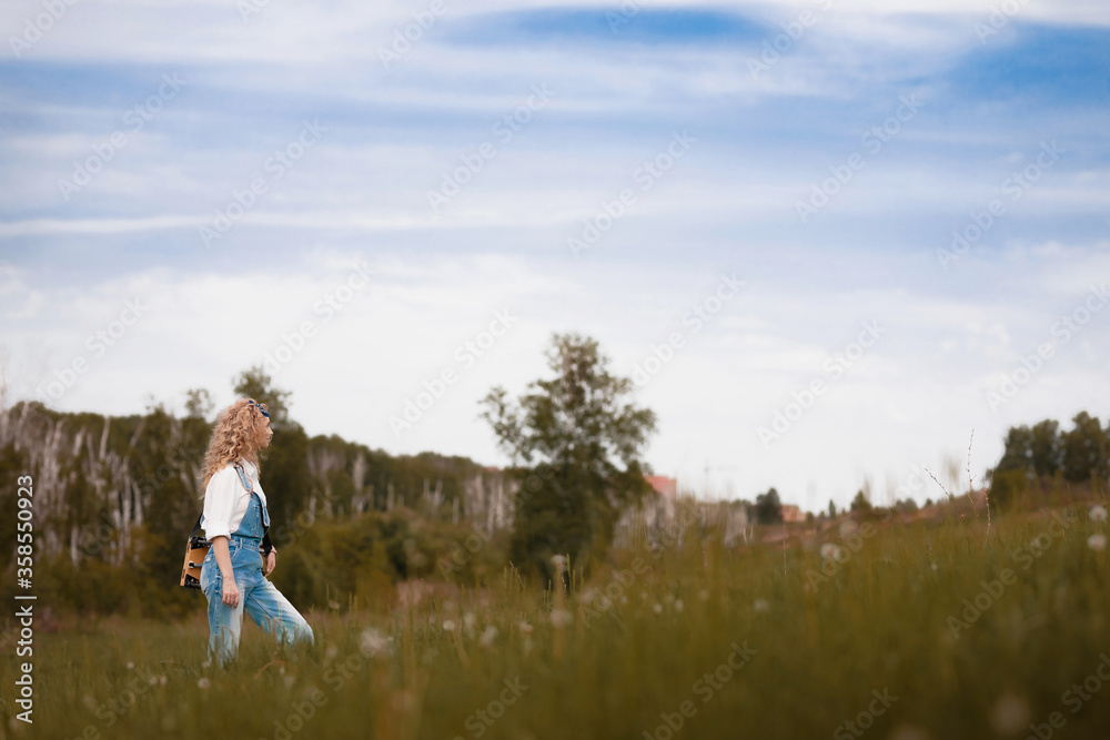 girl with curly hair and denim overalls goes up the forest road in summer
