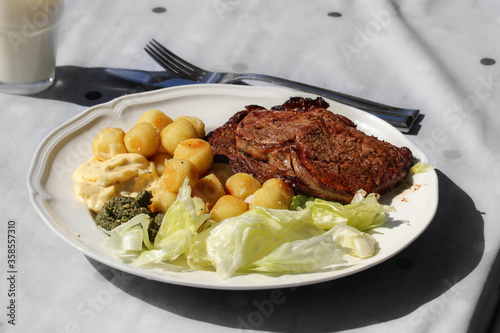A plate with grilled meat, potatoes and sallad sitting on a table in the sunlight