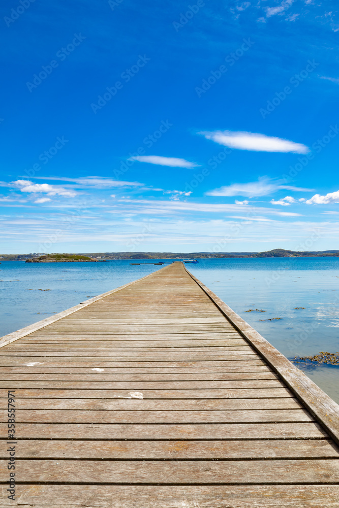 Wooden bridge extending to horizon with ocean and blue sky with clouds Wooden bridge extending to horizon with ocean and blue sky with clouds