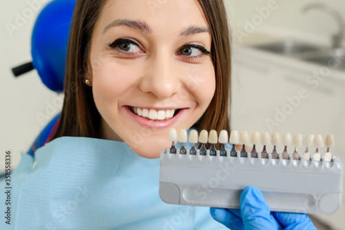 The dentist is checking the color with the tooth color chart of the patient