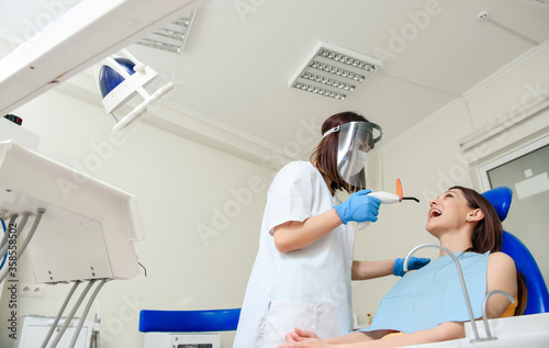 The dentist is using the photopolymer light for finishing the dental filling treatment in dentistry.