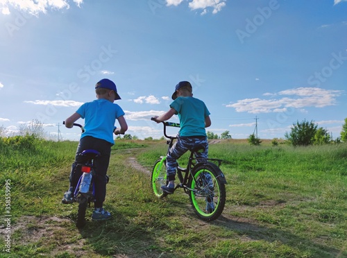 two little boys learn to ride bikes in the field on a sunny day